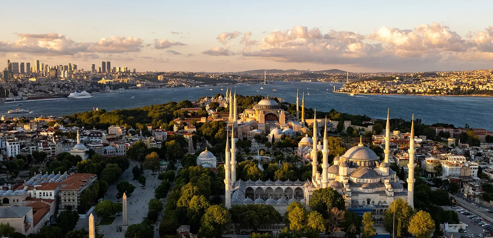 Wide aerial view of Istanbul's historic peninsula with domed mosques beside the Bosphorus and the modern skyline beyond